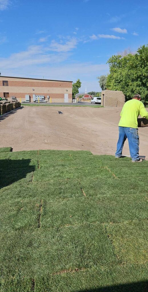 Large open field of freshly laid sod, one worker, and smooth dirt