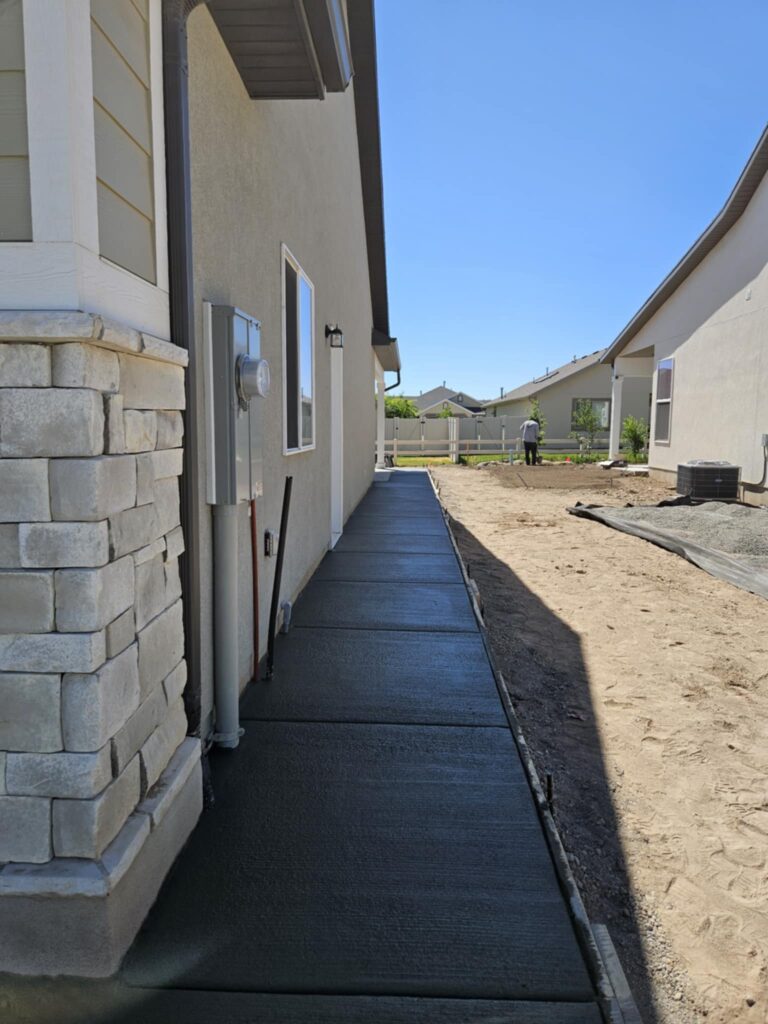 Freshly laid cement walkway against house. Smooth dirt on opposite side of walkway