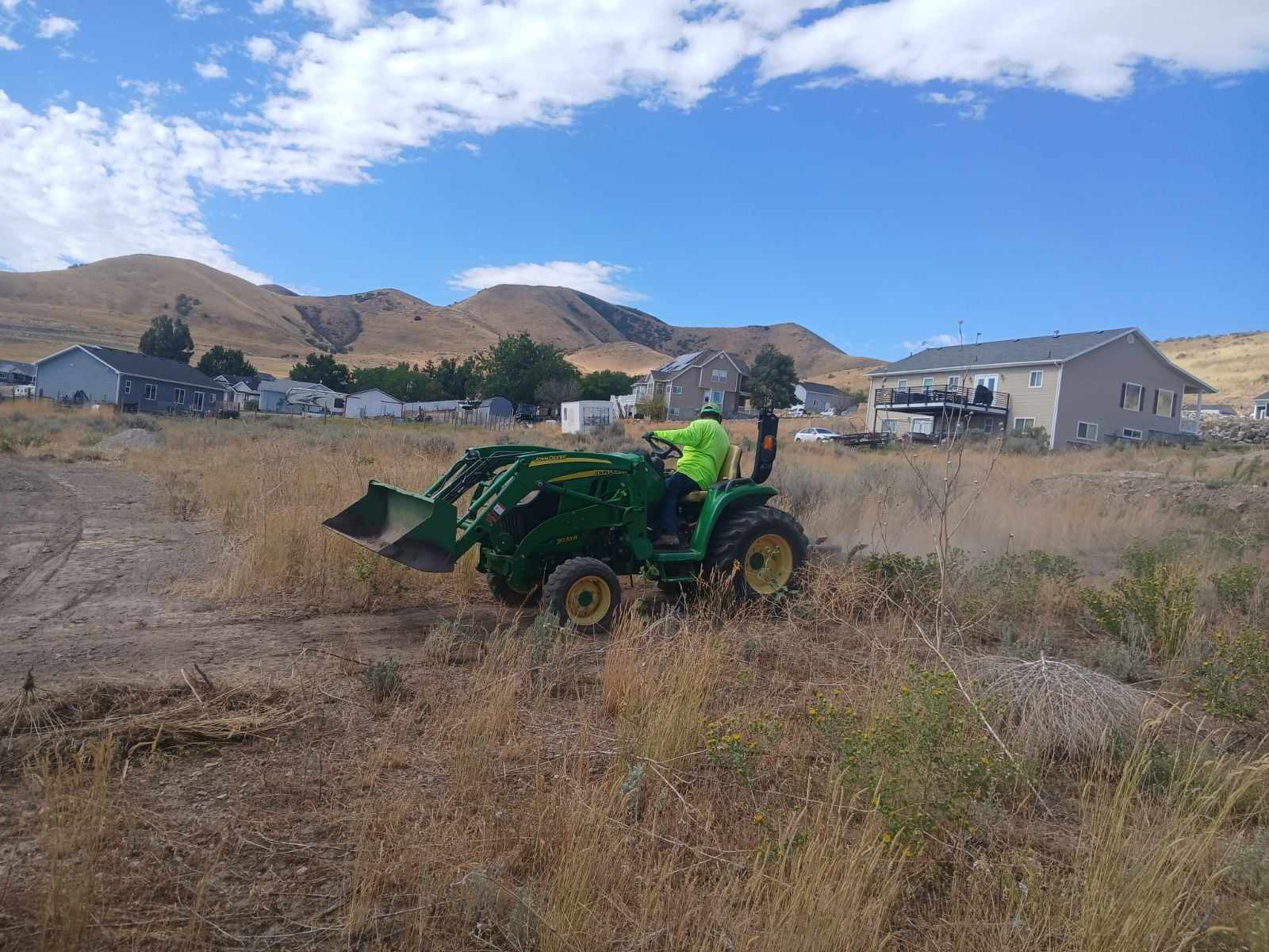 Worker on green tractor full of sagebrush and weeds